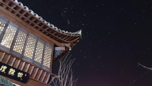 A traditional wooden structure with a tiled roof and illuminated windows. - Dongli Yashe Hotel (Jing County)