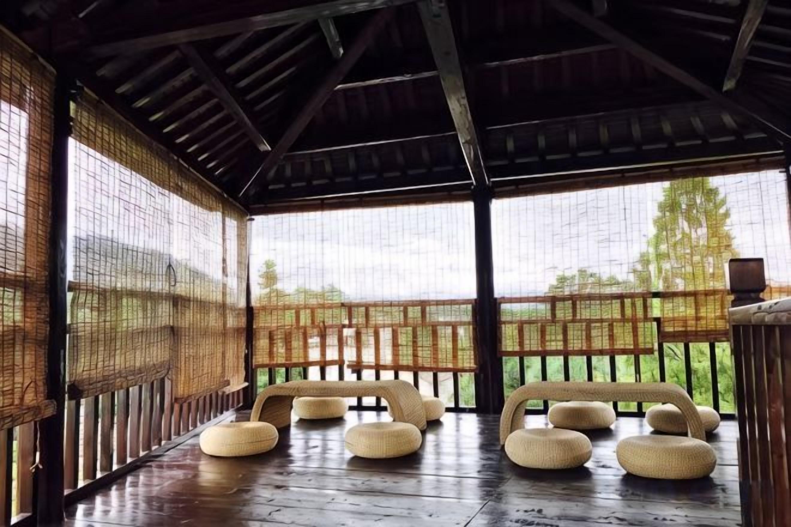 A covered outdoor seating area with a wooden floor and woven screens, surrounded by a wooden fence.