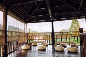 Un espace extérieur aménagé avec des sièges, protégé par un toit, doté d’un plancher en bois et de panneaux décoratifs en fibres tressées, et entouré d’une clôture en bois.