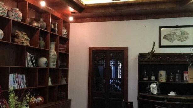 A traditional interior with wooden shelves filled with pottery and books, a dark wooden door, and a bar area with bottles. - Dongli Yashe Hotel (Jing County)