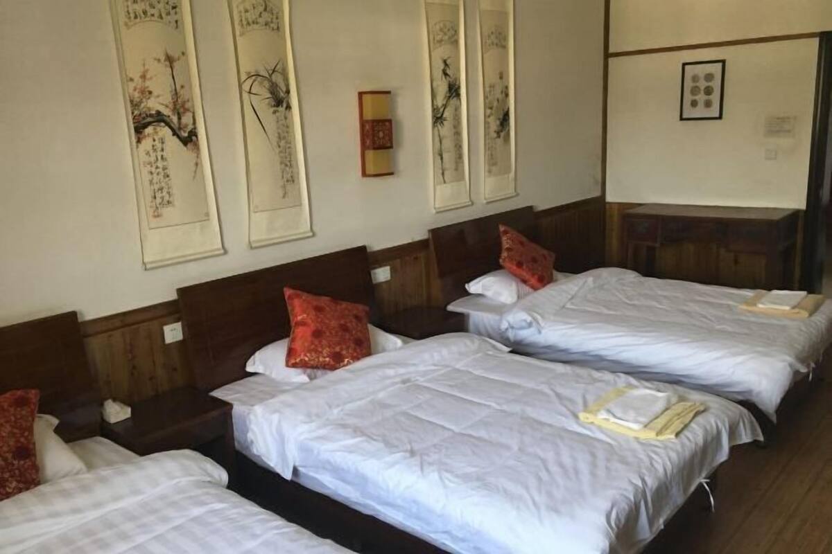 A hotel room with three beds, wooden headboards, and traditional wall art.