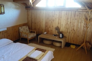Una habitación de madera con una cama, una silla, una mesita y un ventanal.