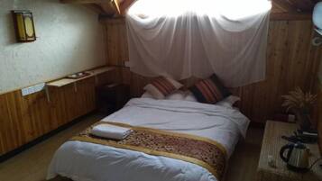 A wooden room with a bed, a nightstand, a lamp, and a window with a white curtain.