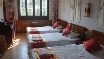 A hotel room with two beds, wooden flooring, a window with decorative glass, and wall-mounted artwork.