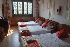 Habitación de hotel con dos camas, suelo de madera, ventana con detalles decorativos y cuadros colgados en la pared.