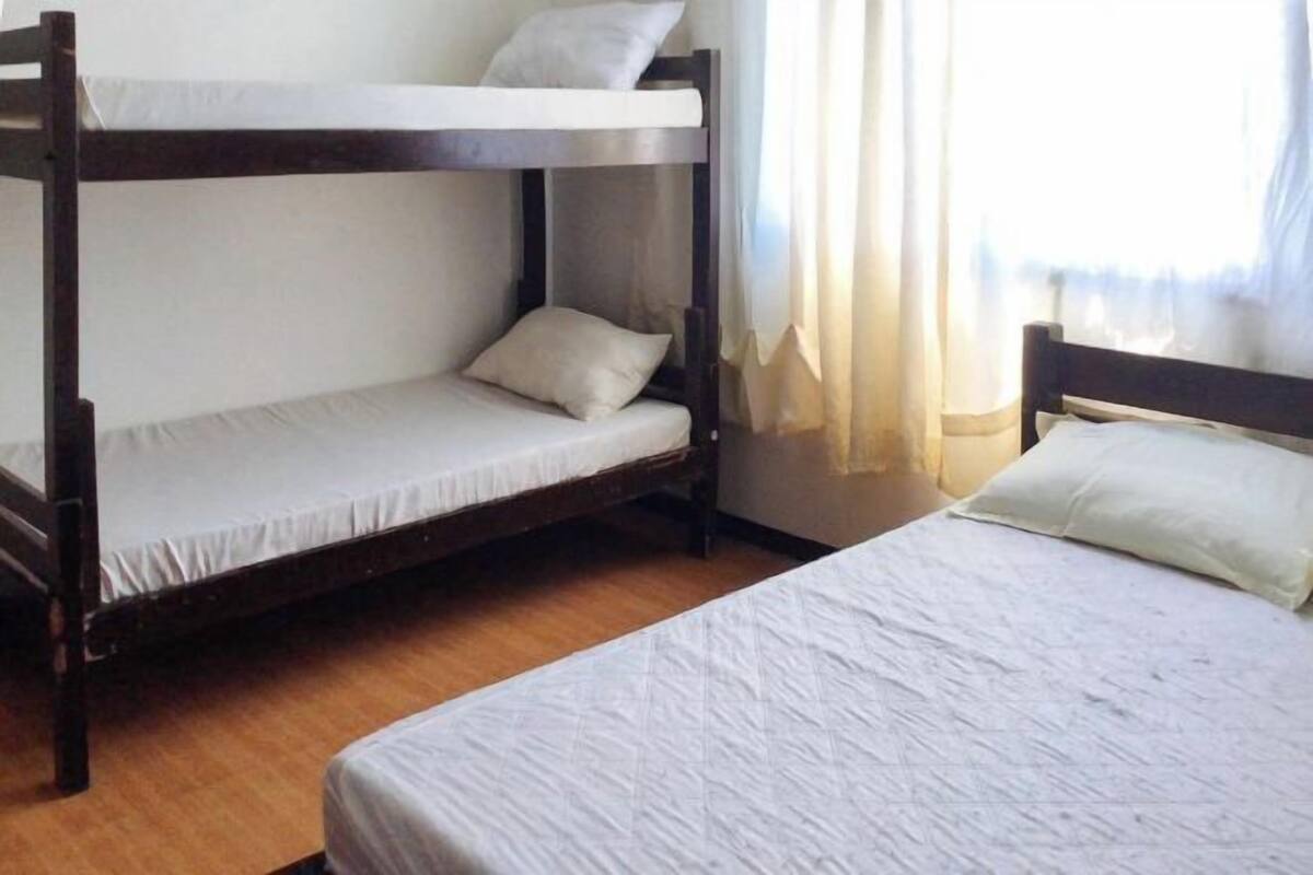 Une chambre avec un lit superposé, un lit simple, une fenêtre avec des rideaux et un plancher en bois.