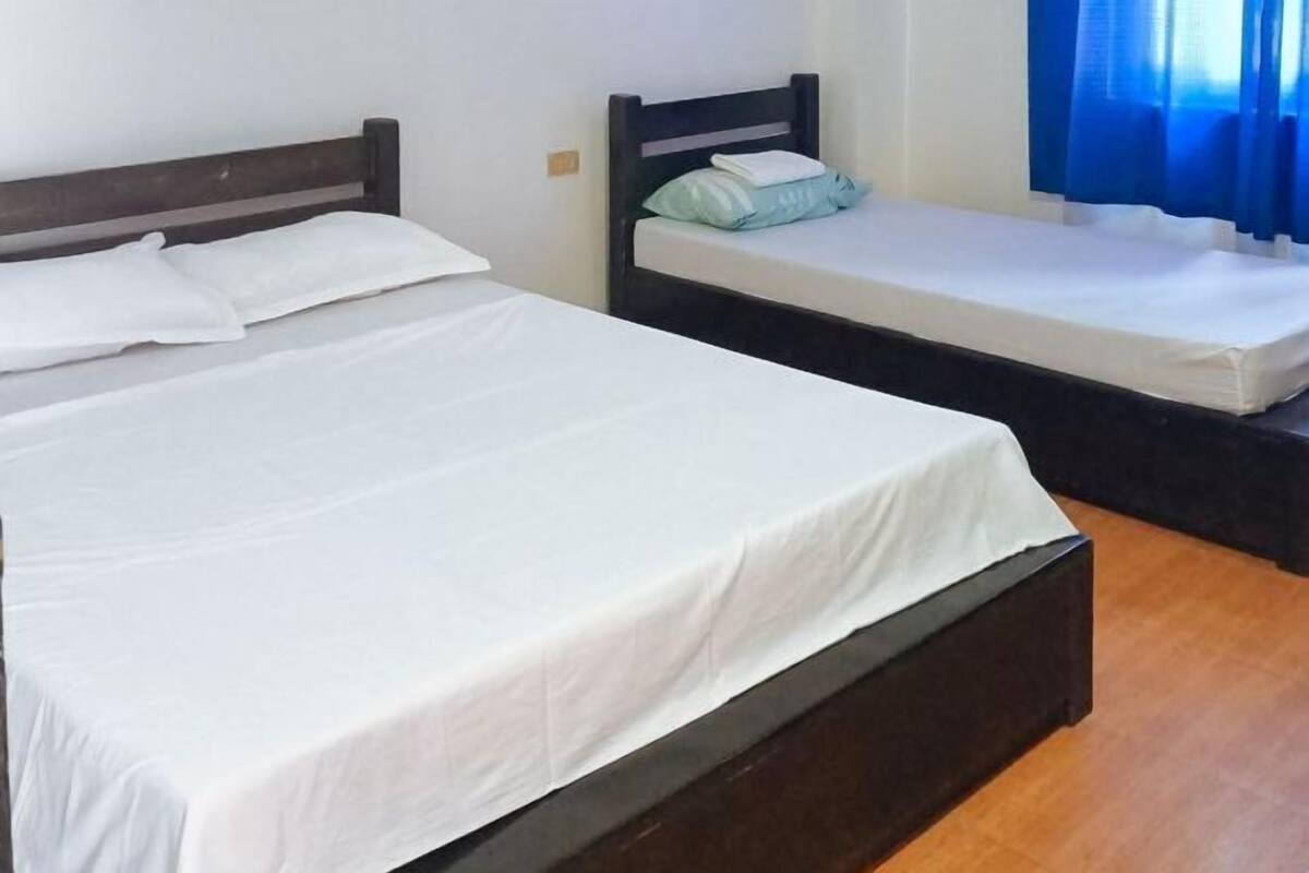 Une chambre avec deux lits simples, chacun doté d’une tête de lit en bois et de draps blancs.