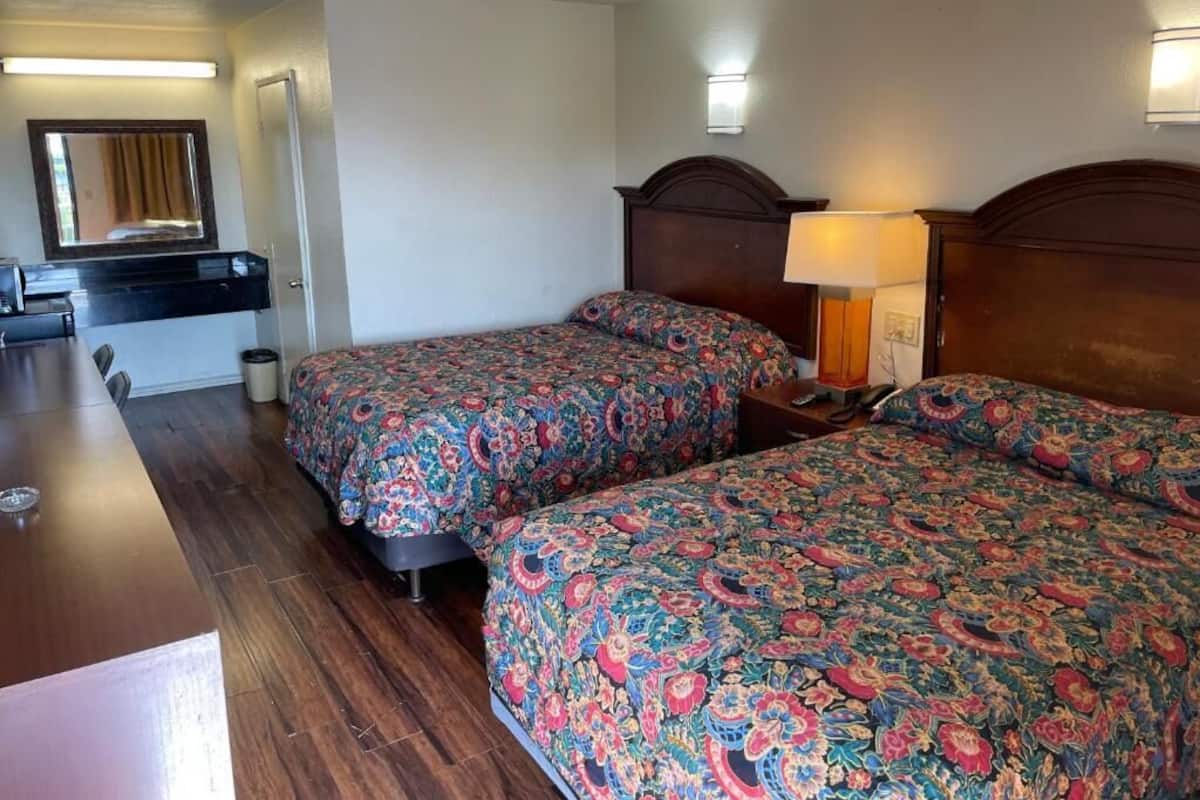 A hotel room with two beds, a wooden dresser, a desk, and a mirror.