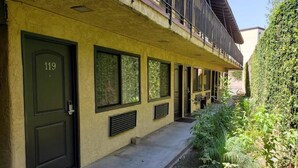 A building with a green door labeled '119', a covered balcony, and a small garden area with plants and a potted plant. - Sierra Inn (South el Monte)