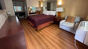 A hotel room with a large bed, a sofa, a desk, and a mirror. - Sierra Inn (South el Monte)