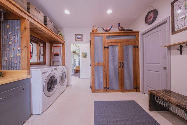 A laundry area with a washing machine and dryer, wooden shelves, and a bench.