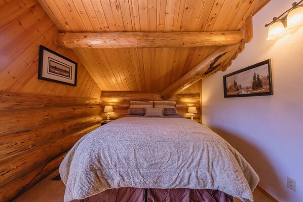 Een gezellig houten slaapkamer met een bed, houten wanden en twee ingelijste foto’s.