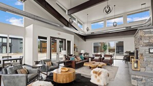 A spacious living room with leather sofas, a stone fireplace, and large windows allowing natural light. - Whitefish All Seasons Getaway (Whitefish)