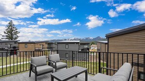 A deck with outdoor furniture, a view of a mountain range, and a row of cabins. - Whitefish All Seasons Getaway (Whitefish)