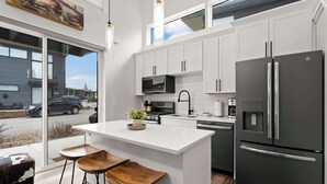 A modern kitchen with white cabinets, a stainless steel refrigerator, and a large island with stools. - Whitefish All Seasons Getaway (Whitefish)