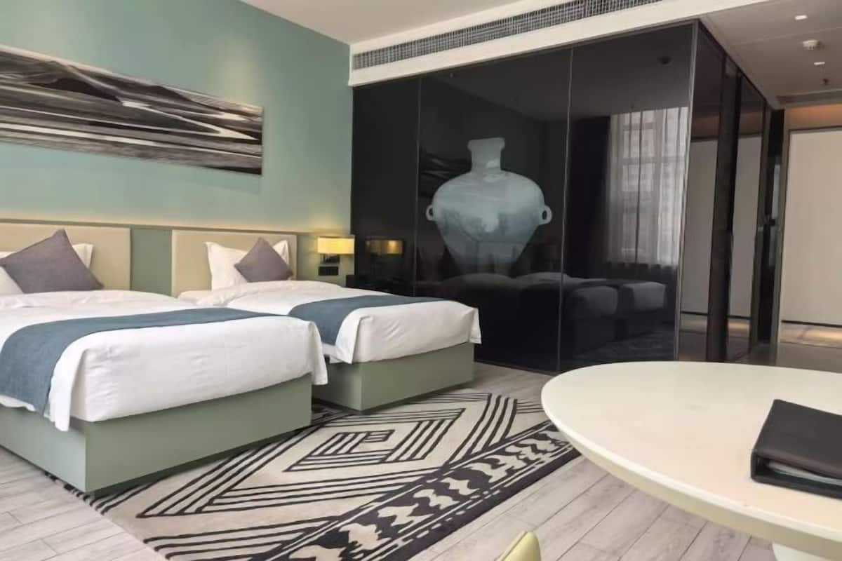 Habitación de hotel con dos camas, una mesa redonda, un jarrón grande y un cuadro abstracto moderno.