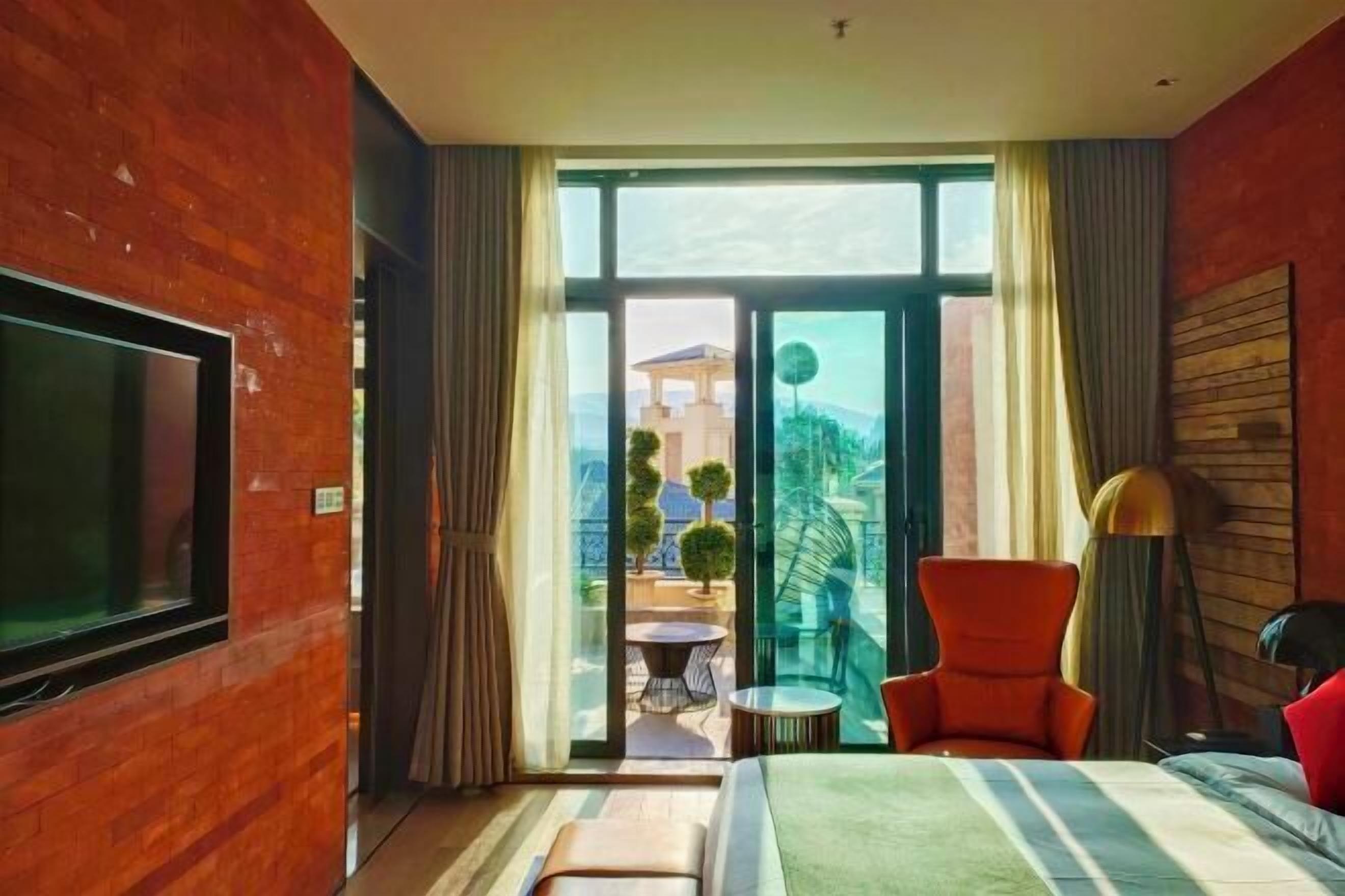A modern hotel room with a large bed, a TV, a balcony with a table and chairs, and a view of the city.