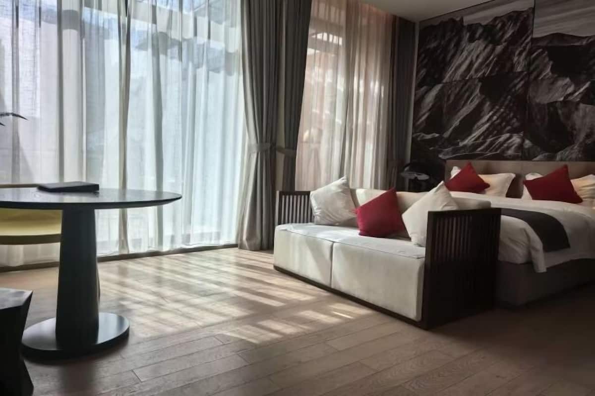 Una habitación de hotel moderna con sofá cama, una mesa redonda y un gran mural abstracto en la pared.