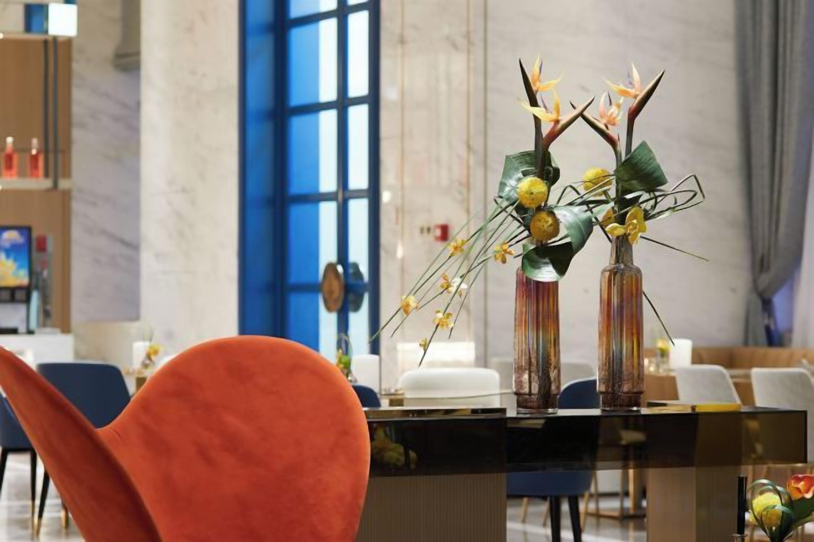 Un espace d’accueil avec un comptoir en verre, des chaises et un vase rempli de fleurs.