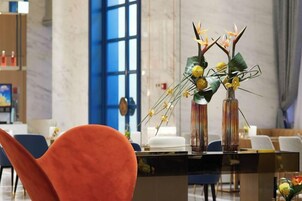 Un área de recepción con mostrador de vidrio, sillas y un jarrón con flores.