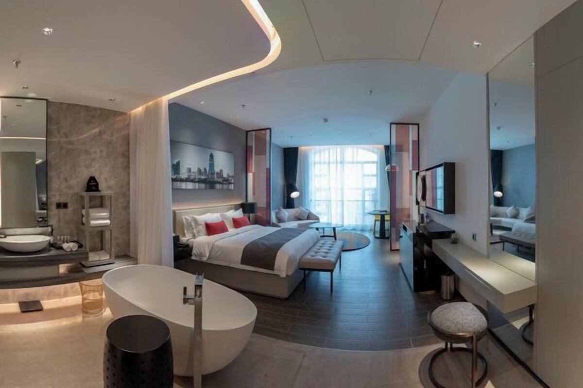 Una habitación de hotel moderna con una cama grande, una zona de estar separada, una bañera y un televisor.