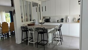 Una cocina moderna con armarios blancos, una isla central con taburetes y un comedor con sillas estampadas.