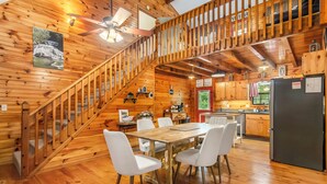 Interior de una cabaña de madera con comedor, cocina y escalera.