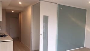 Una habitación con puerta corredera, kitchenette con estufa y piso de color claro.