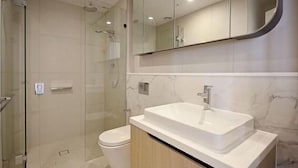Un baño moderno con ducha envuelta en vidrio, un lavabo blanco y un espejo grande sobre el mueble.
