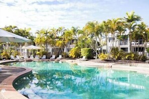 Ein Swimmingpool, umgeben von Palmen und Liegestühlen.