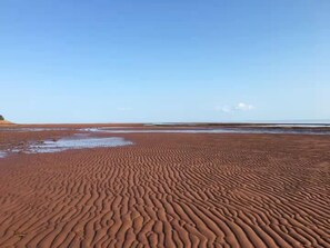 A sandy beach with rippled patterns, a clear sky, and a distant horizon.