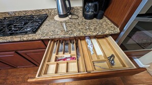 Una cocina con encimera de granito, estufa a gas, cafetera y organizador de cajones con utensilios.