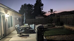 Un patio con mesa y sillas, una parrilla y luces colgantes.