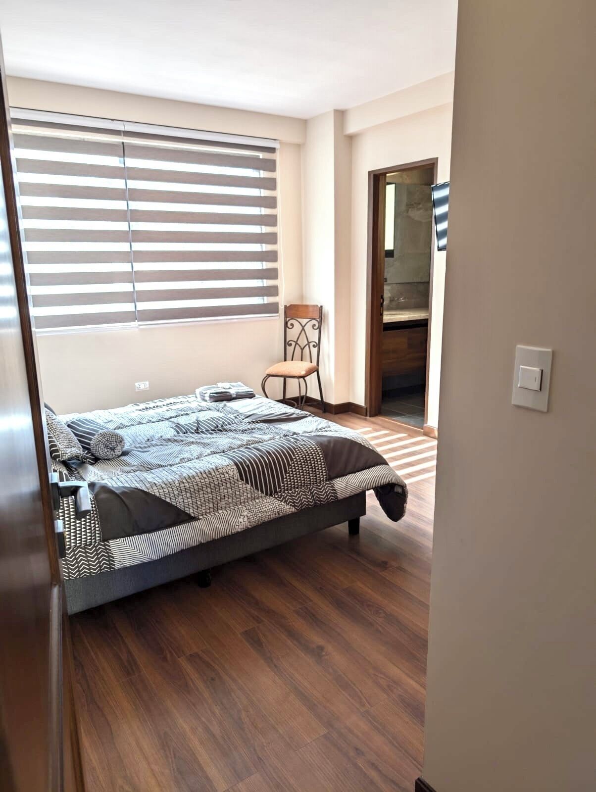 Ein Schlafzimmer mit einem Bett, einem Sessel, einem Fenster mit Jalousien und Holzboden.