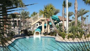 Une piscine avec un toboggan, des palmiers et un bâtiment doté d’un balcon.
