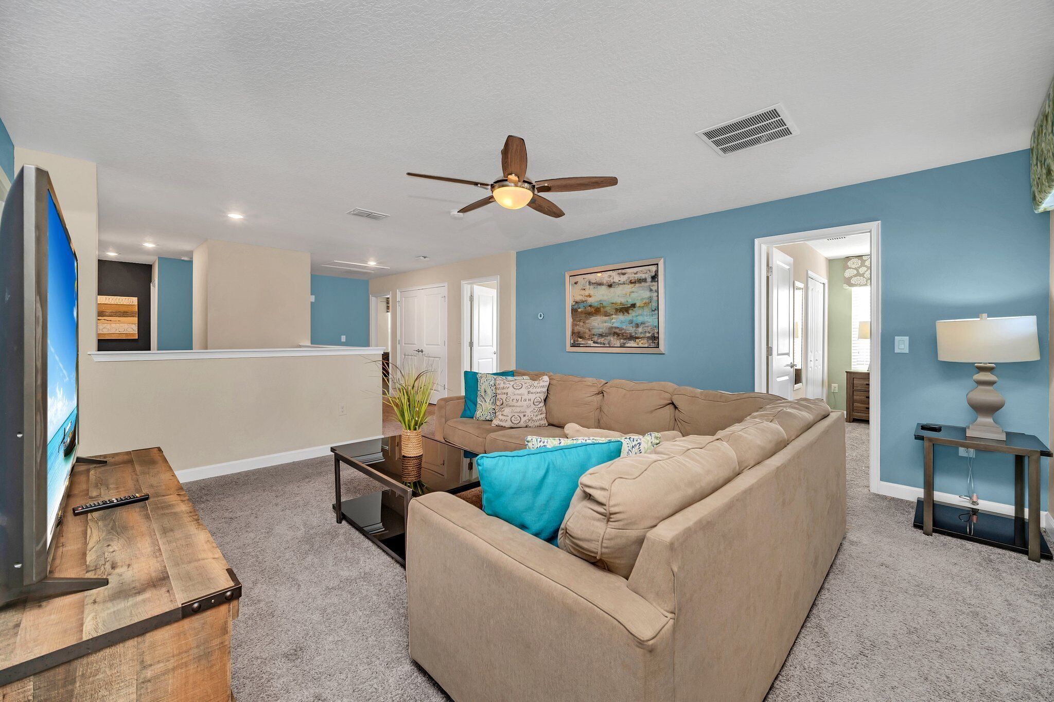 A living room with a beige sofa, a coffee table, a TV, and a ceiling fan.