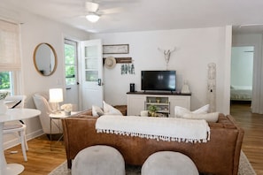 Ein modernes Wohnzimmer mit einem braunen Sofa, weißen Kissen, einem Fernseher und einem dekorativen Schädel an der Wand.