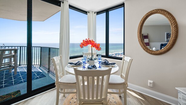 A dining area with a view of the ocean, a round mirror, and a table set for two.