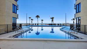 A swimming pool with clear blue water, surrounded by palm trees and modern buildings.