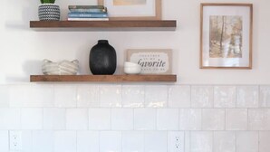 Une cuisine avec des meubles blancs, un plan de travail en marbre et un pare-feu en carreaux.