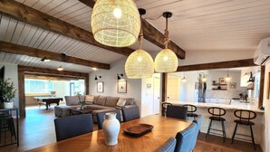 Un vaste espace de vie comprenant une table à manger en bois, des chaises bleues et un grand vase. On y trouve également deux lampes suspendues en osier et un canapé à l’arrière-plan.