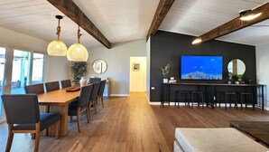 Un vaste espace de vie comprenant une table à manger en bois, des chaises, un canapé et un coin bar avec des tabourets.