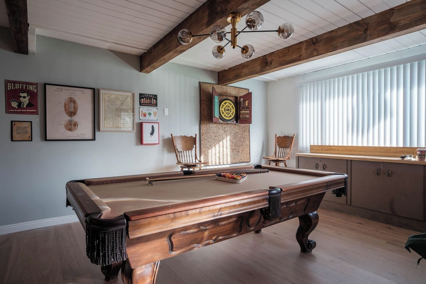 Een pooltafel in een ruimte met houten balken, ingelijste certificaten aan de muur en een raam met zonwering.