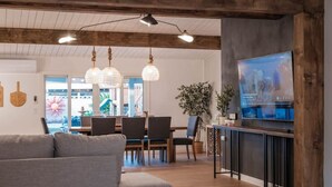 Un salon moderne avec une table de billard, un canapé gris, des poutres en bois et un téléviseur.