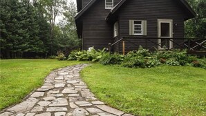 Un camino de piedra que lleva a una casa de madera oscura con un porche y una pequeña terraza.