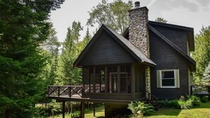 Una cabaña con chimenea de piedra, un balcón y rodeada de árboles.