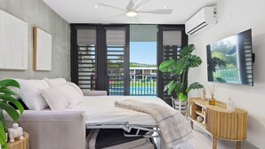 Un dormitorio moderno con cama, ventilador de techo, ventana grande y vistas al exterior.
