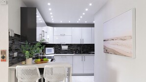 Una cocina moderna con armarios blancos, salpicadero negro y un comedor con dos sillas blancas.