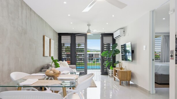 Un comedor moderno con una mesa de vidrio, sillas blancas y vistas al exterior.