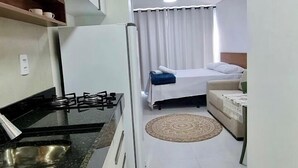 A compact hotel room with a kitchenette, a bed, a sofa, and a small rug. - Villas do Porto - 212 by La Playa (Ipojuca)